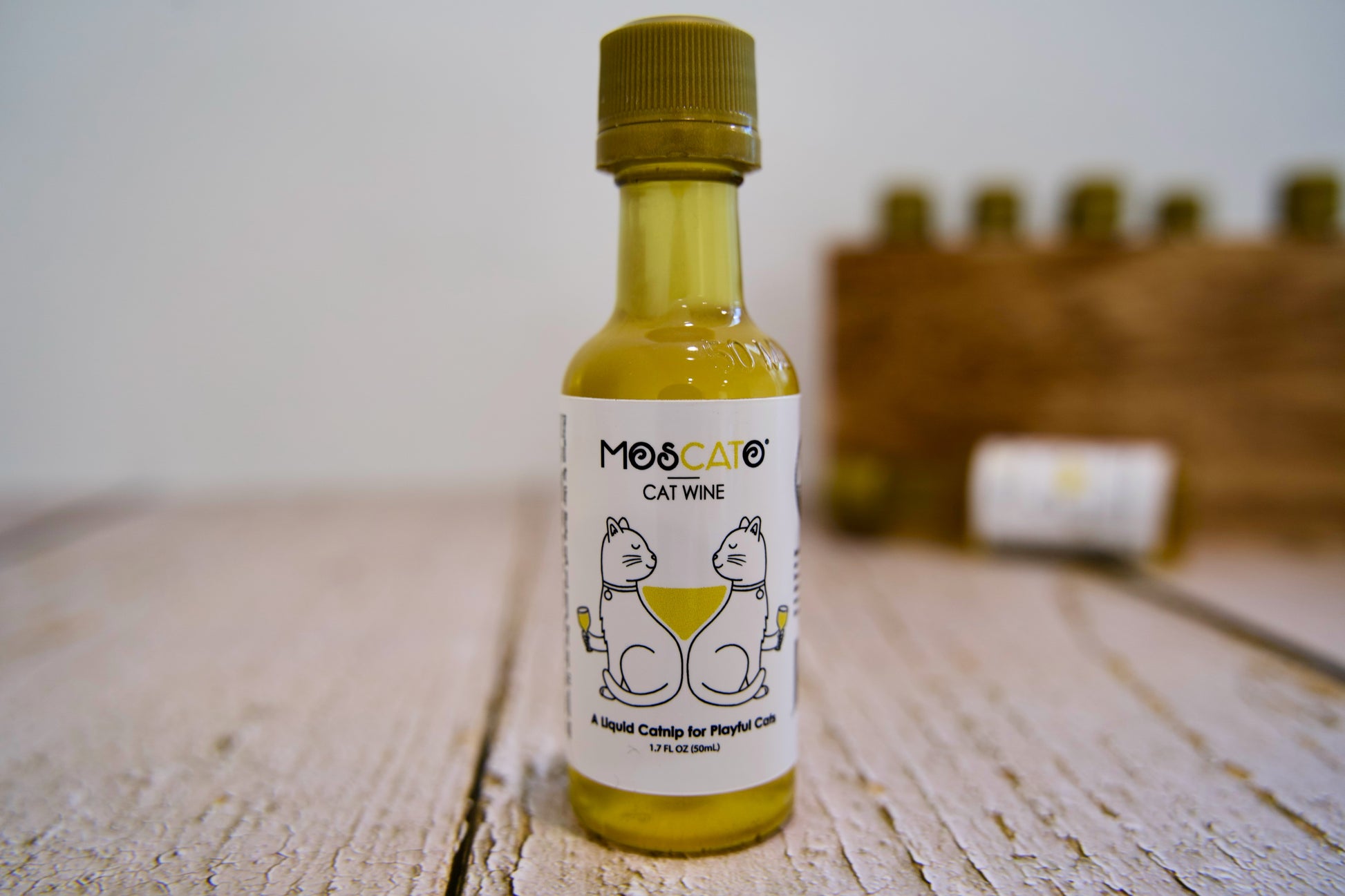 Bouteille de vin pour chats MosCato posée sur une surface en bois, avec un arrière-plan flou.