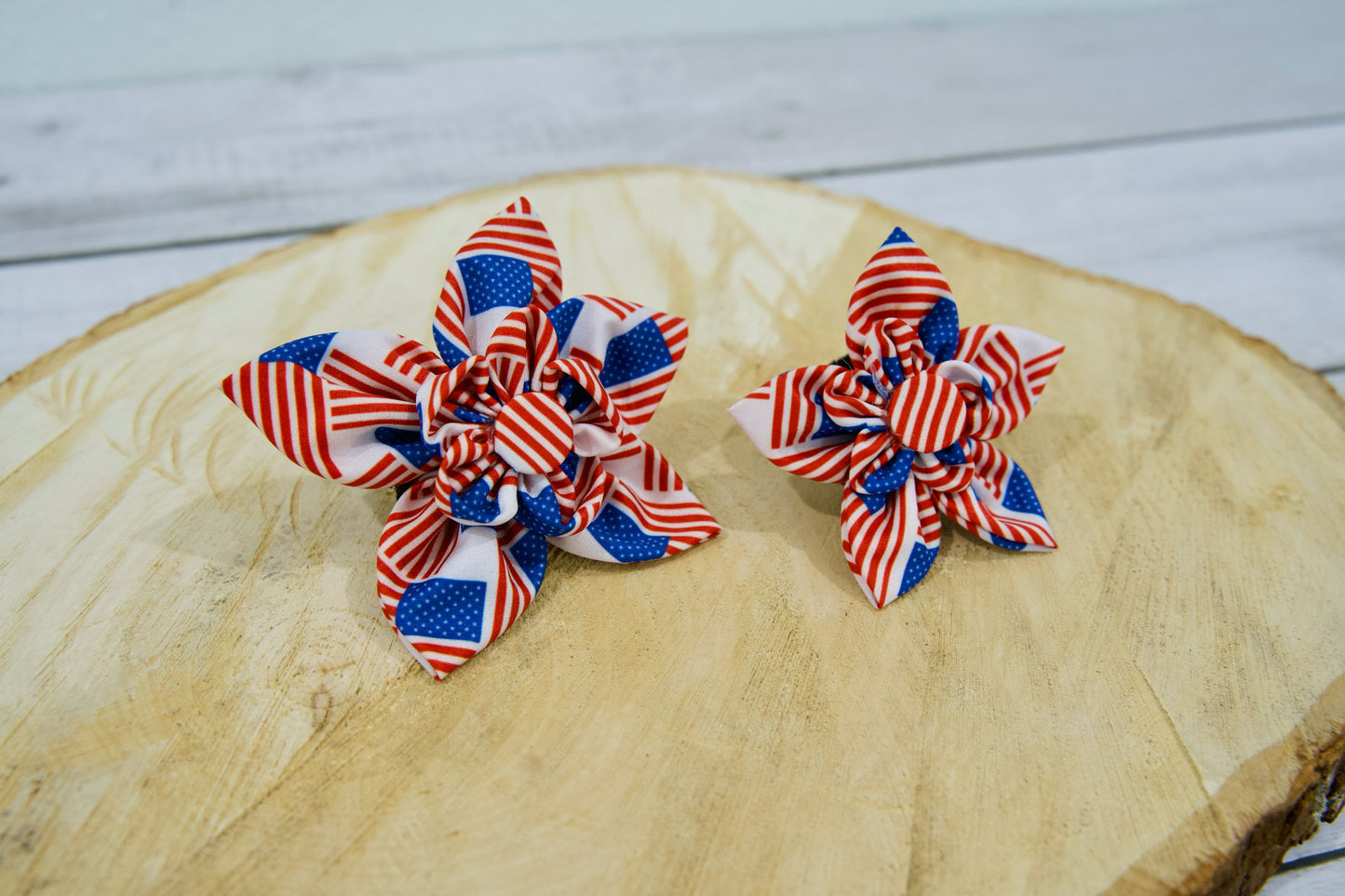 Deux accessoires patriotiques en forme de fleur pour collier de chien ou chat, posés sur une surface en bois.