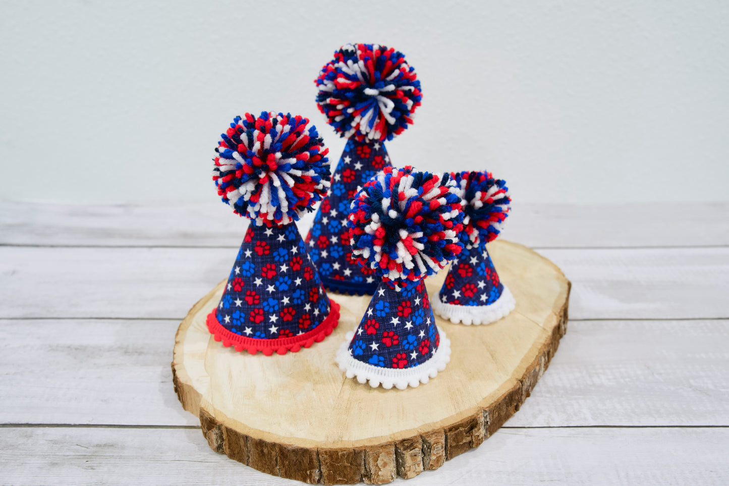 Chapeaux de fête et pompons aux couleurs rouge, blanc et bleu pour animaux, disposés sur une surface en bois.
