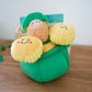 Plush toy for dogs with a leprechain in a green pot of gold on a wooden surface.