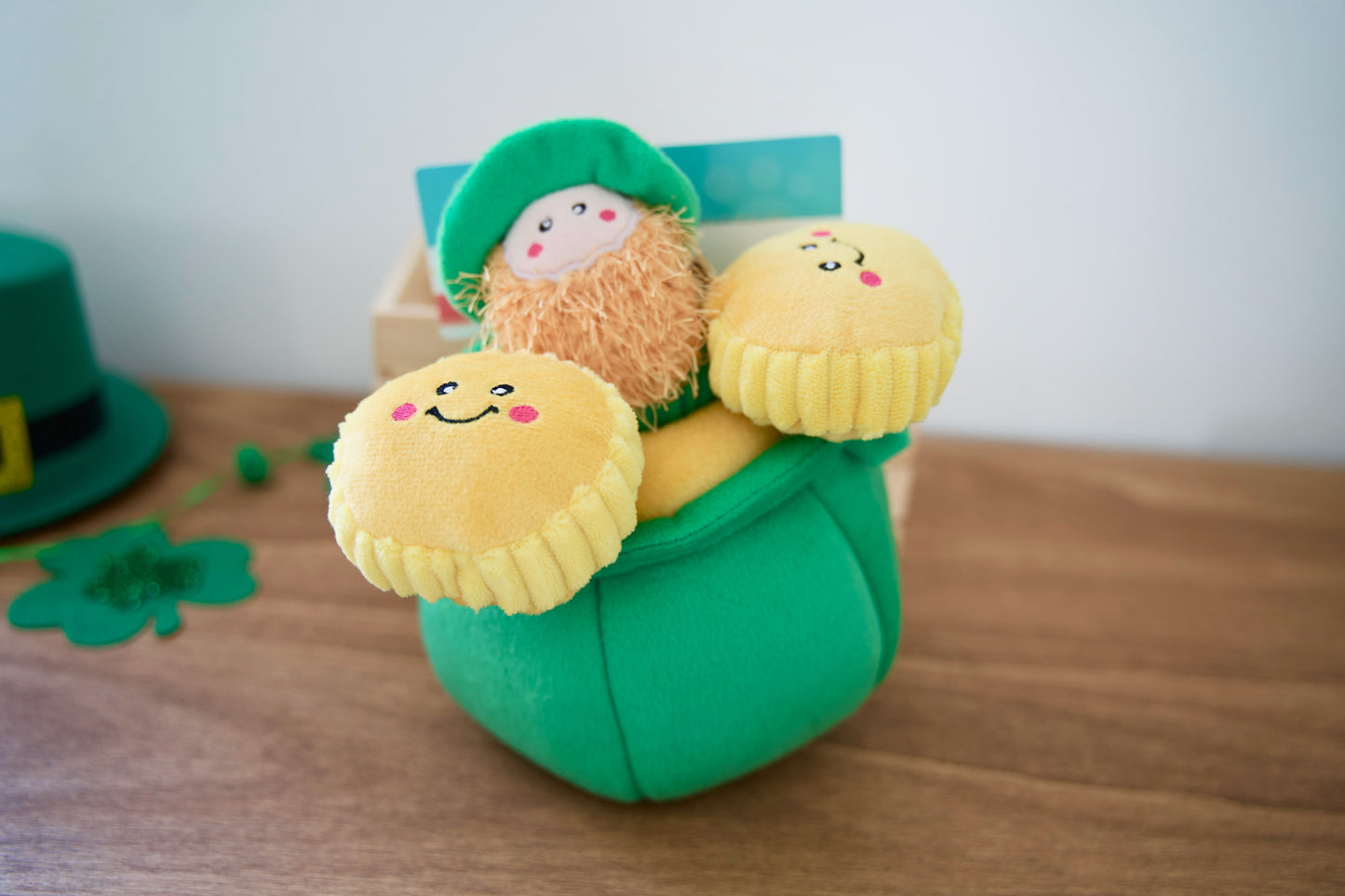 Plush toy for dogs with a leprechain in a green pot of gold on a wooden surface.