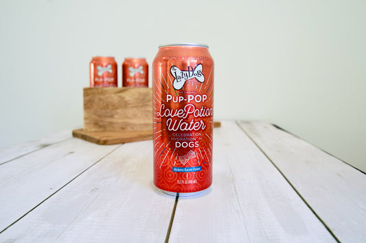 Red can of Pup-Pop Love Potion Water for dogs on a wooden surface.|Une canette rouge d'eau pour chien Pup-Pop Love Potion posée sur une surface en bois.