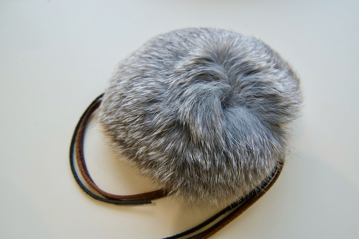 Gray fur pom-pom with leather whiskers cat toy on a white background.