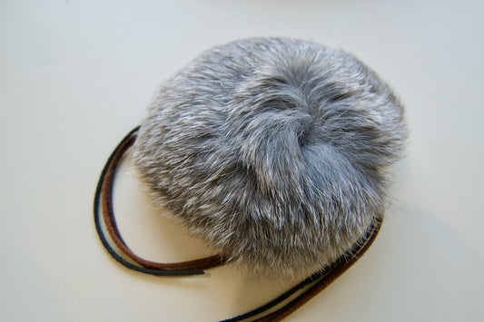 Gray fur pom-pom with leather whiskers cat toy on a white background.|Jouet pour chat en forme de pompon de fourrure grise avec des moustaches en cuir, sur fond blanc.