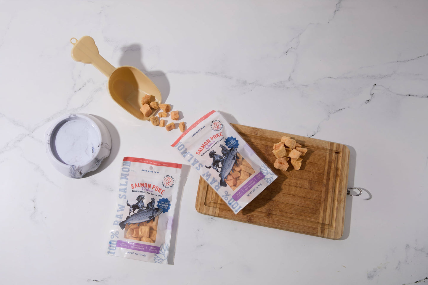 Deux paquets de friandises au saumon pour chiens et chats sont disposés sur une surface en marbre blanc.