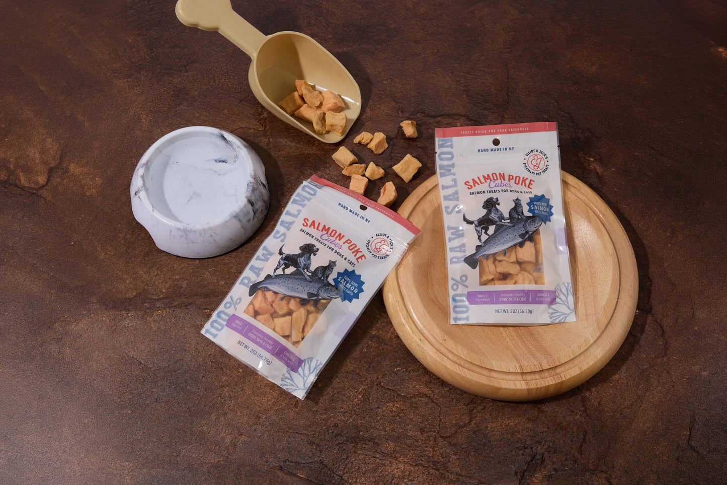 Deux paquets de friandises « Salmon Poke » pour chiens et chats sont présentés sur une surface texturée brun foncé.