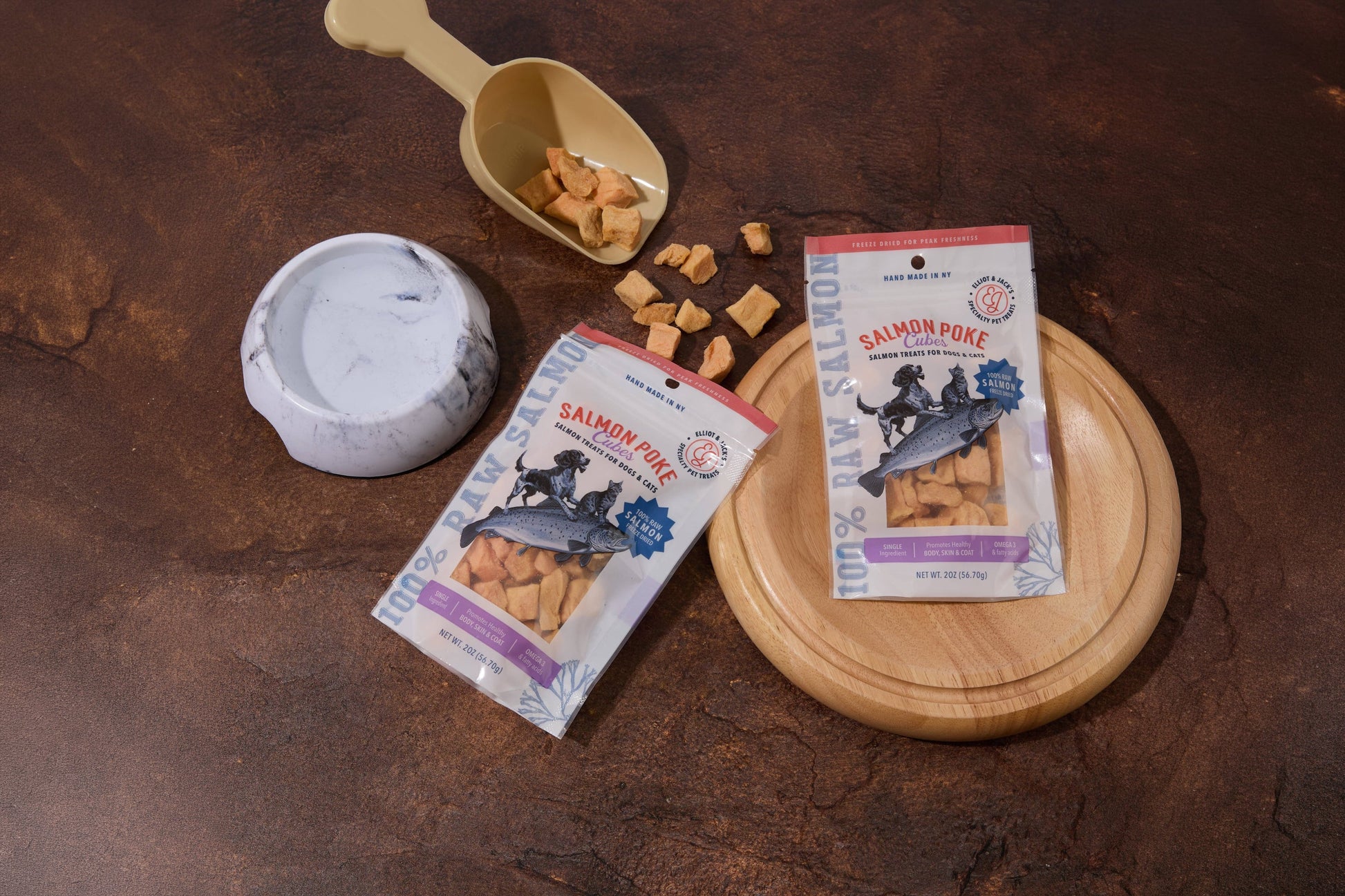 Deux paquets de friandises « Salmon Poke » pour chiens et chats sont présentés sur une surface texturée brun foncé.