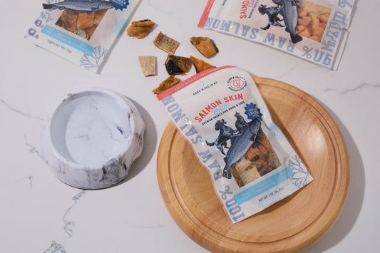 A package of salmon skin snacks for dogs and cats is displayed on a round wooden.|Un paquet de friandises à base de peau de saumon pour chiens et chats est présenté sur un support rond en bois.