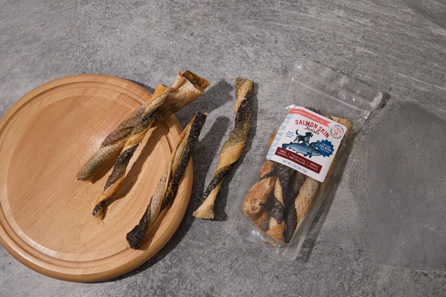 Four spiral-cut salmon roe snacks for dogs and cats displayed on a round wooden board.
