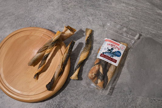 Four spiral-cut salmon roe snacks for dogs and cats displayed on a round wooden board.|Quatre friandises en spirale à base d'œufs de saumon pour chiens et chats, présentées sur une planche ronde en bois.