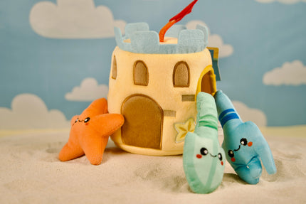 Chien jouant avec un jouet château de sable en peluche rempli de pièces sur le thème de la plage.
