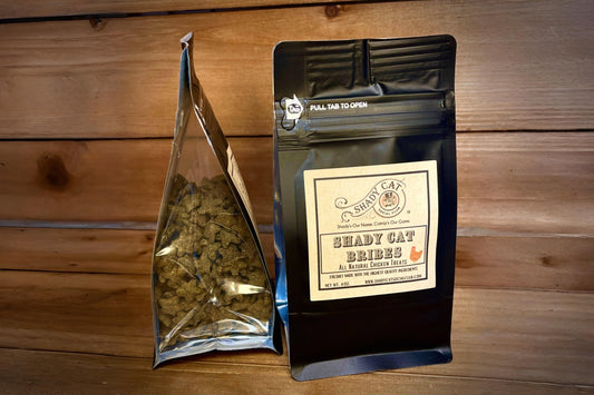 Two packages of Shady Cat Bribes on a wooden surface.|Deux paquets de friandises Shady Cat posés sur une surface en bois.