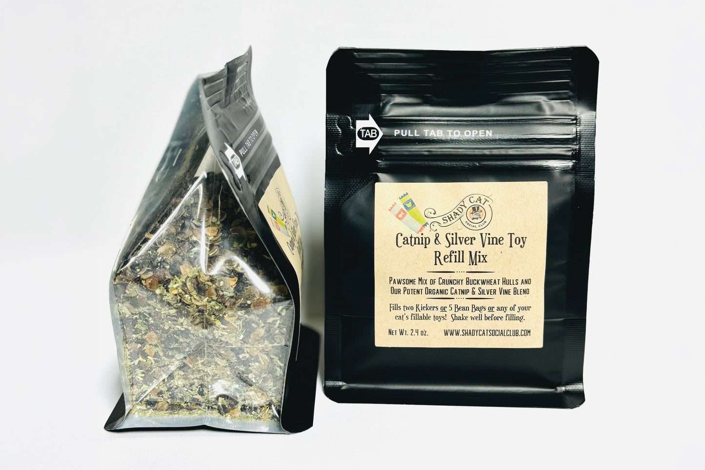 Deux sachets de produits sur fond blanc uni : un sachet transparent à fond plat contenant des herbes séchées en vrac et un sachet noir refermable portant l'étiquette « Catnip & Silver Vine Toy Refill Mix » et une étiquette frontale beige.