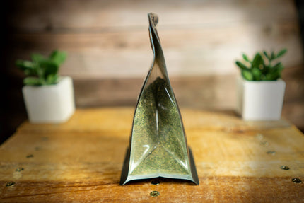 A clear pouch filled with fine ground catnip blend, standing upright on a rustic wooden table.