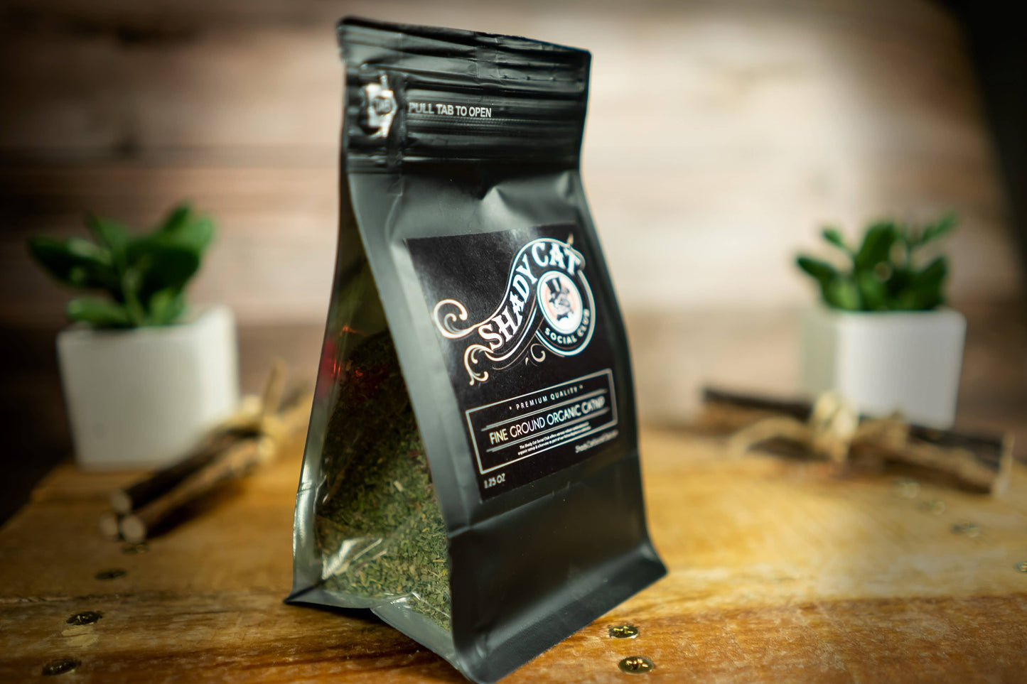 A black stand-up pouch of Shady Cat Organic Cat Enrichment, labeled 'The Ground Organic Chip', standing on a rustic wooden surface.