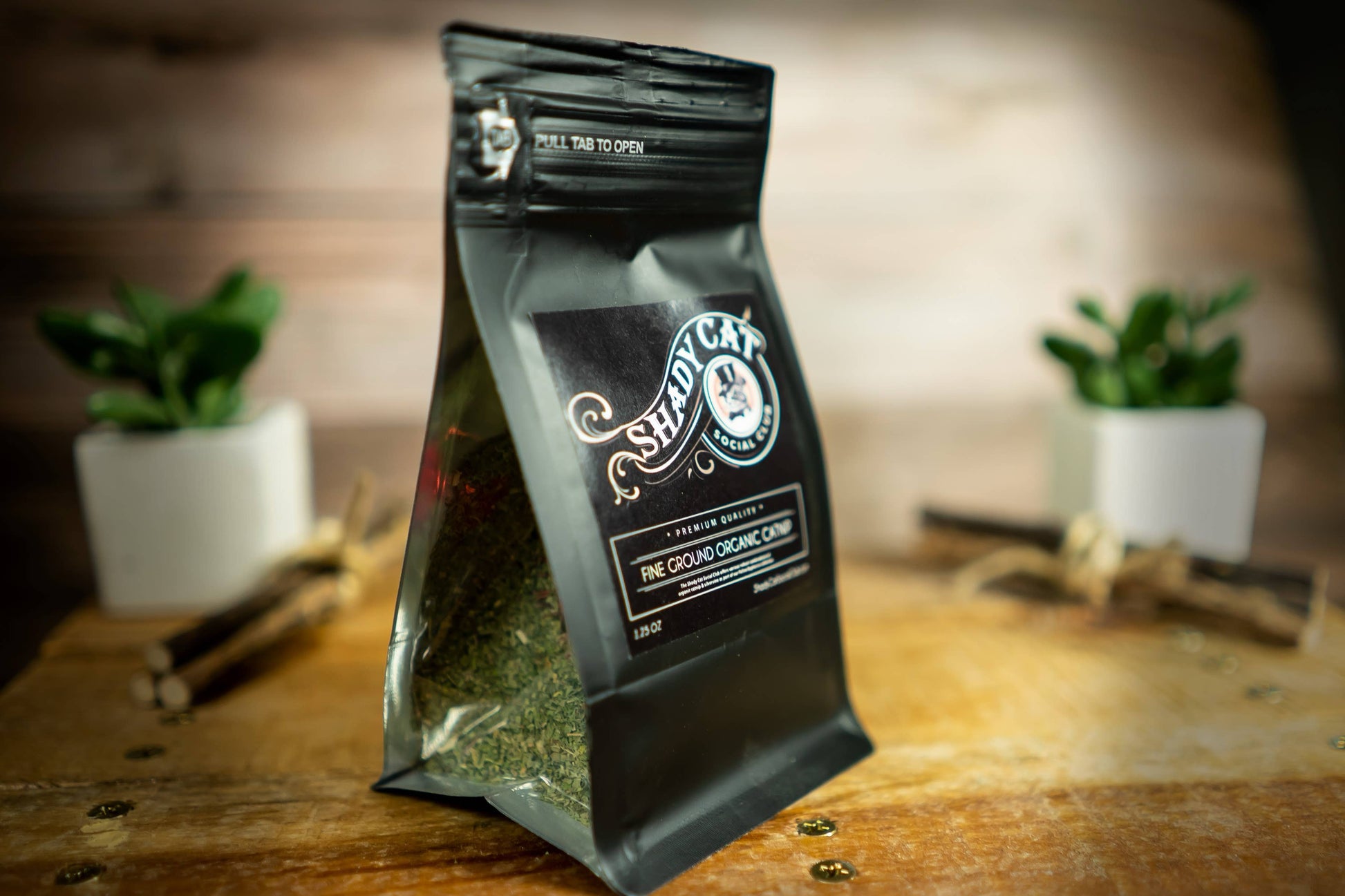 A black stand-up pouch of Shady Cat Organic Cat Enrichment, labeled 'The Ground Organic Chip', standing on a rustic wooden surface.