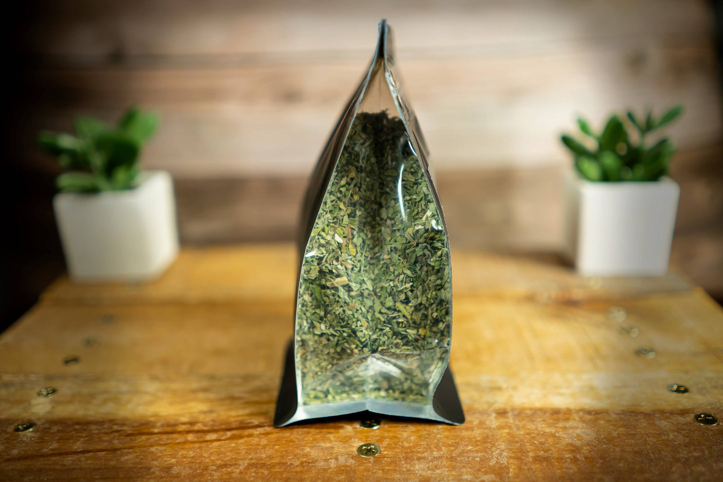 Un sachet souple transparent tenant debout, rempli de feuilles et de fleurs de cataire séchées, posé sur une surface en bois.