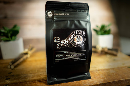 Shady Cat organic catnip and valerian blend bag on a wooden surface with a blurred background.|Un sachet de mélange biologique d'herbe à chat et de valériane de la marque Shady Cat posé sur une surface en bois, avec un arrière-plan flou.