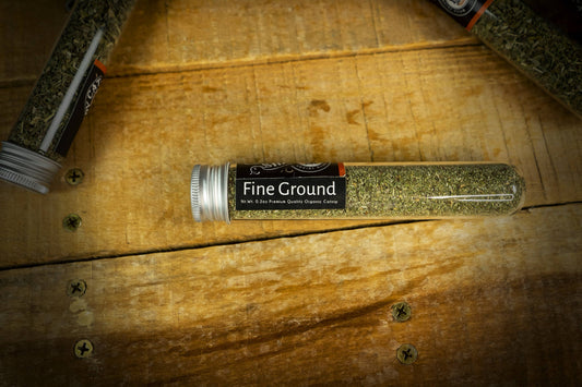 Tubular container labeled Fine Ground Catnip on a wooden surface.|Un récipient tubulaire étiqueté herbe à chat finement moulue posé sur une surface en bois.