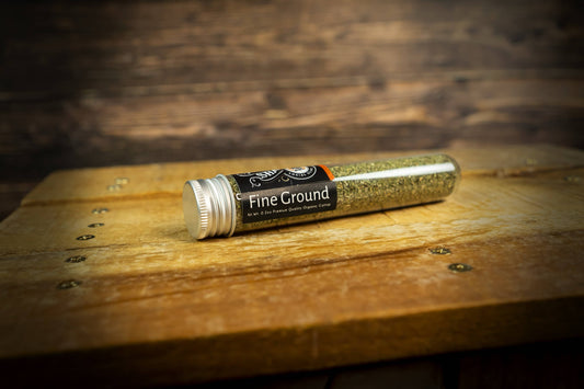 Tube of fine ground catnip fine on a wooden surface with a blurred background.|Tube de cataire finement moulue, posé sur une surface en bois, avec un arrière-plan flou.