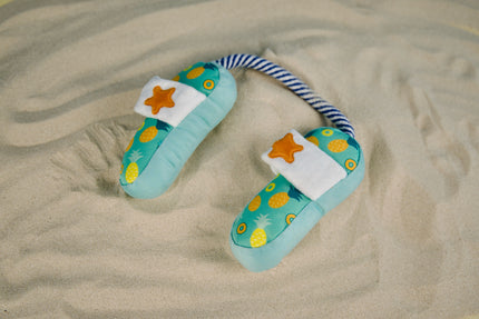 The playful dog slipper toy rests on warm sand, ready for beachside tugging and tail-wagging fun.