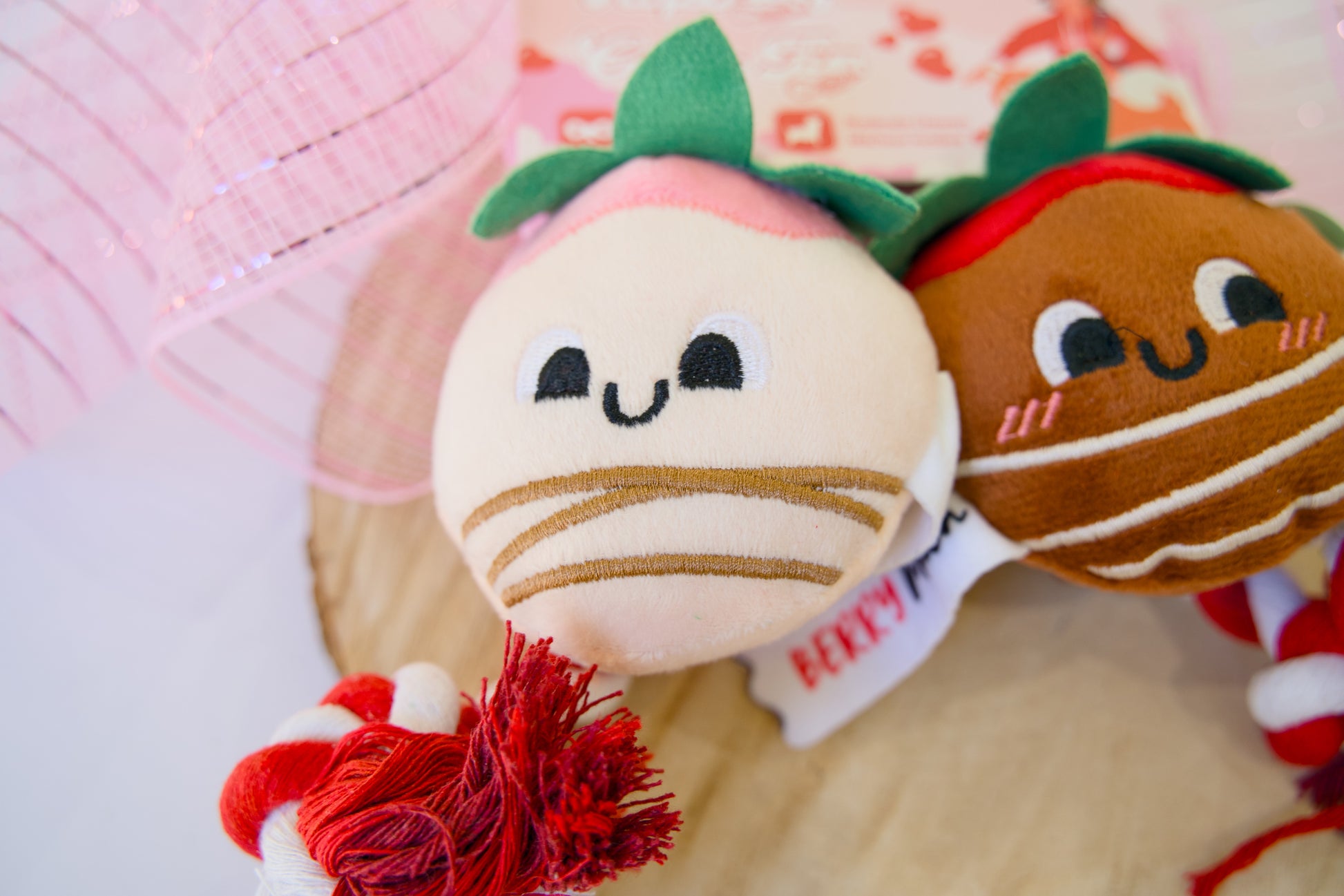 Two plush dog toys resembling berries with a red tassel on a light background.