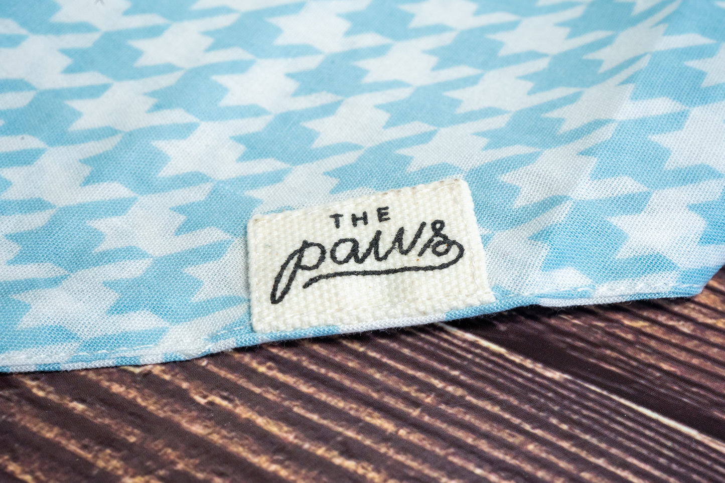 Gros plan sur le logo The Paws sur bandana pour chien avec motifs de pied-de-poule.