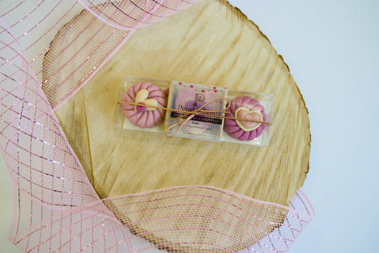 Pink and purple dog truffle in clear packaging on a wooden surface with decorative pink netting.|Friandise pour chien rose et violette dans un emballage transparent, posée sur une surface en bois avec un filet décoratif rose.