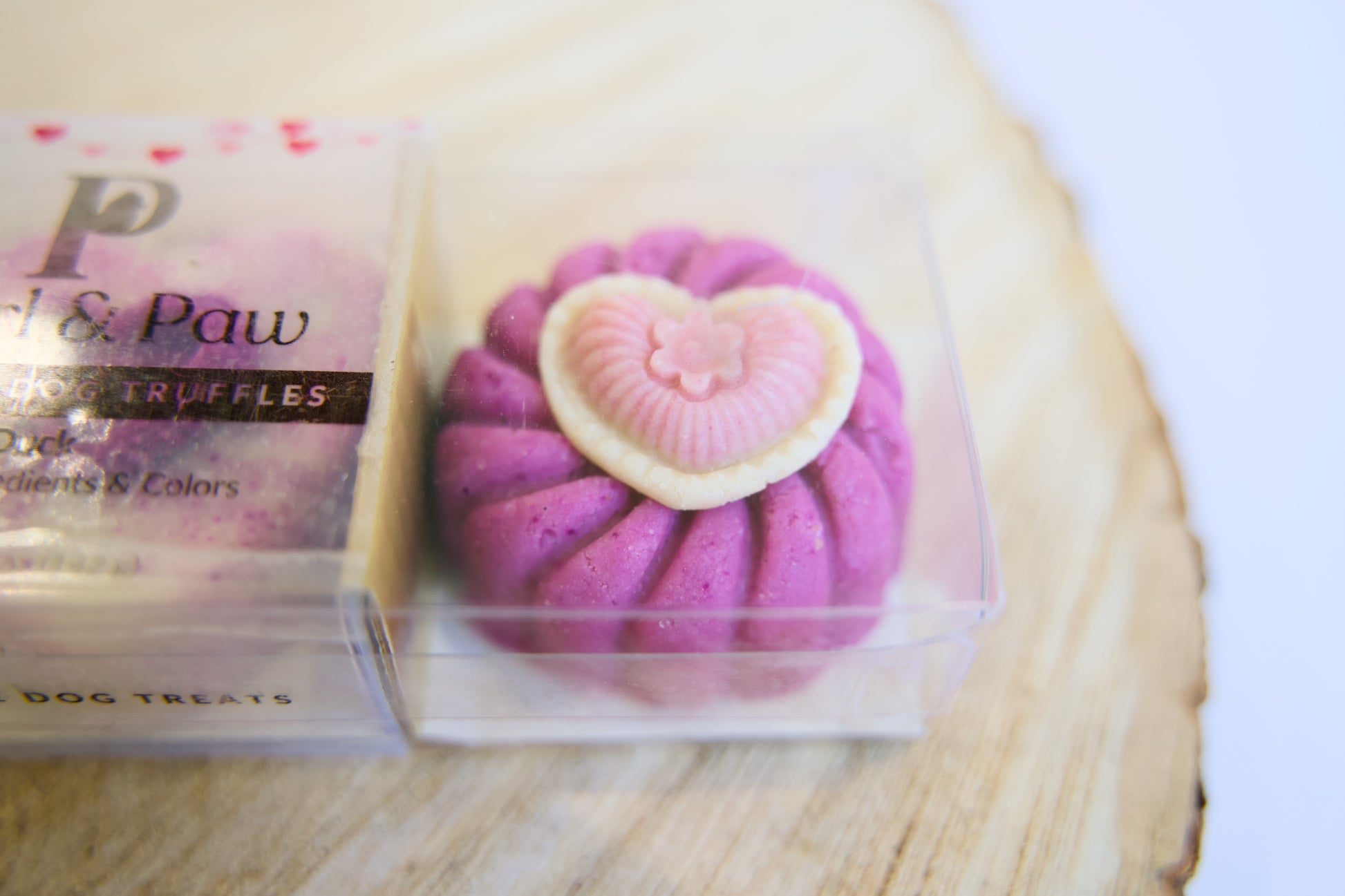 Purple dog treat with heart design in a clear packaging on a wooden surface.