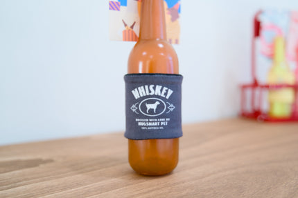 Bouteille pour chien avec une étiquette de whisky posée sur une surface en bois.