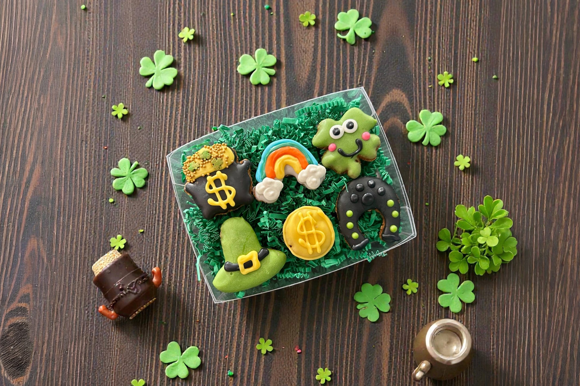 Decorative dog cookies with green icing, gold coins, a rainbow, and shamrocks on a wooden surface.