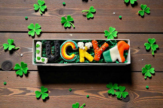 Colorful LUCKY Dog candy arrangement on a wooden surface with shamrock decorations.|Présentation de bonbons colorés LUCKY Dog sur une surface en bois avec des décorations en forme de trèfle.