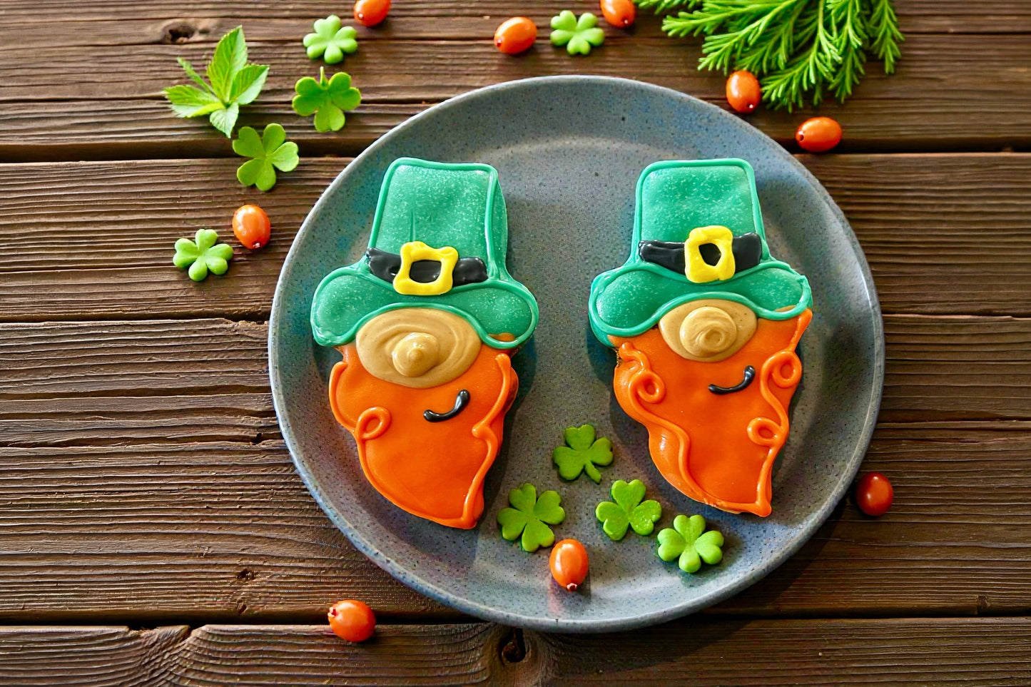 Two leprechaun-shaped cookies for dog on a plate with shamrock leaves.
