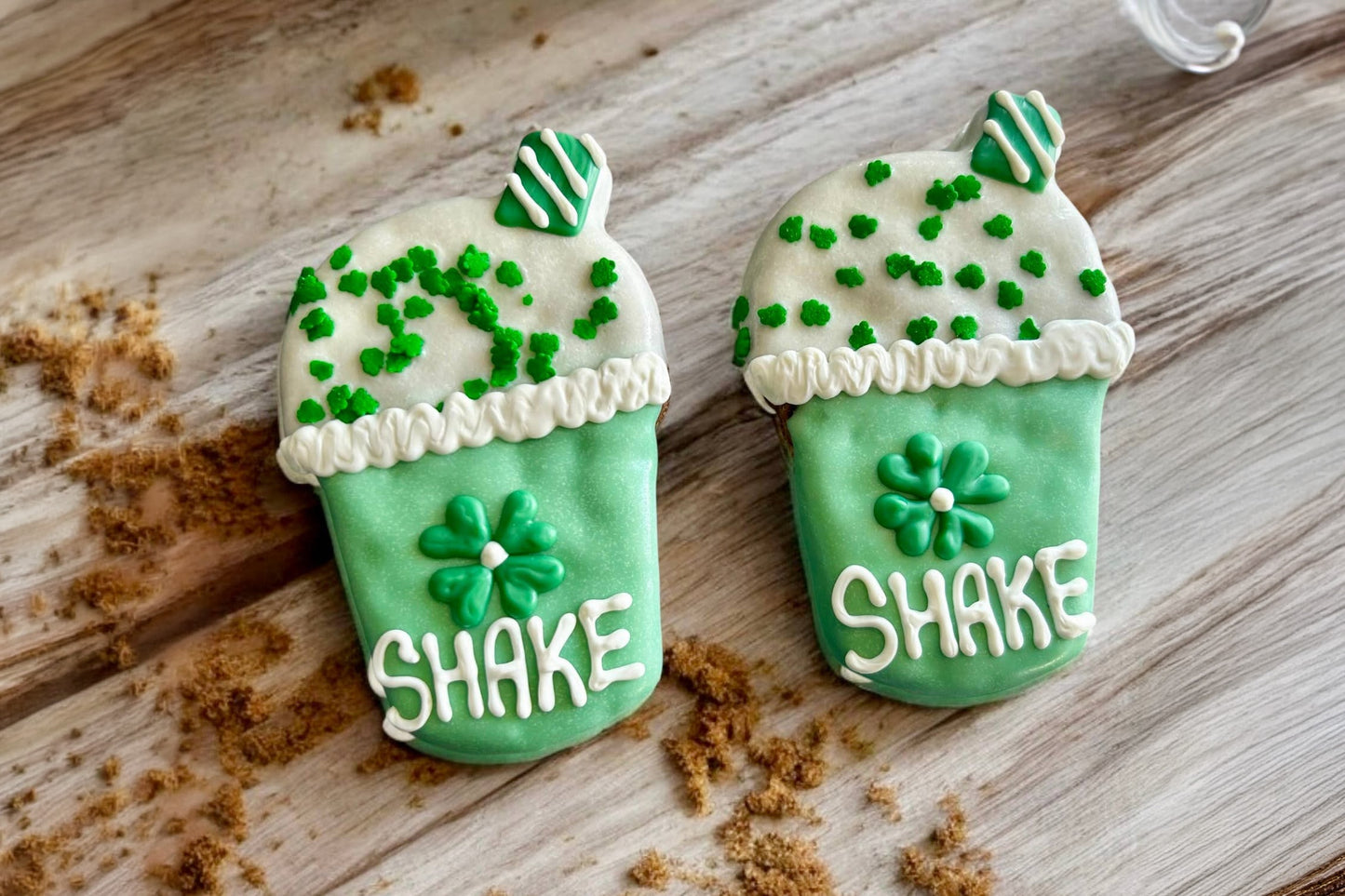 Two green ice cream shake cookies for dogs with white text on a wooden surface.