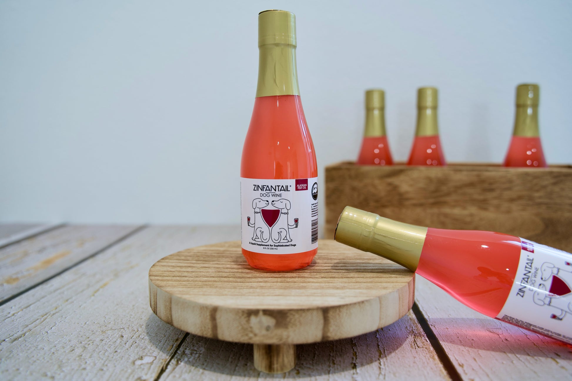 Une bouteille de vin rosé pour chiens, coiffée d'un bouchon doré, posée sur un support en bois, avec d'autres bouteilles en arrière-plan.